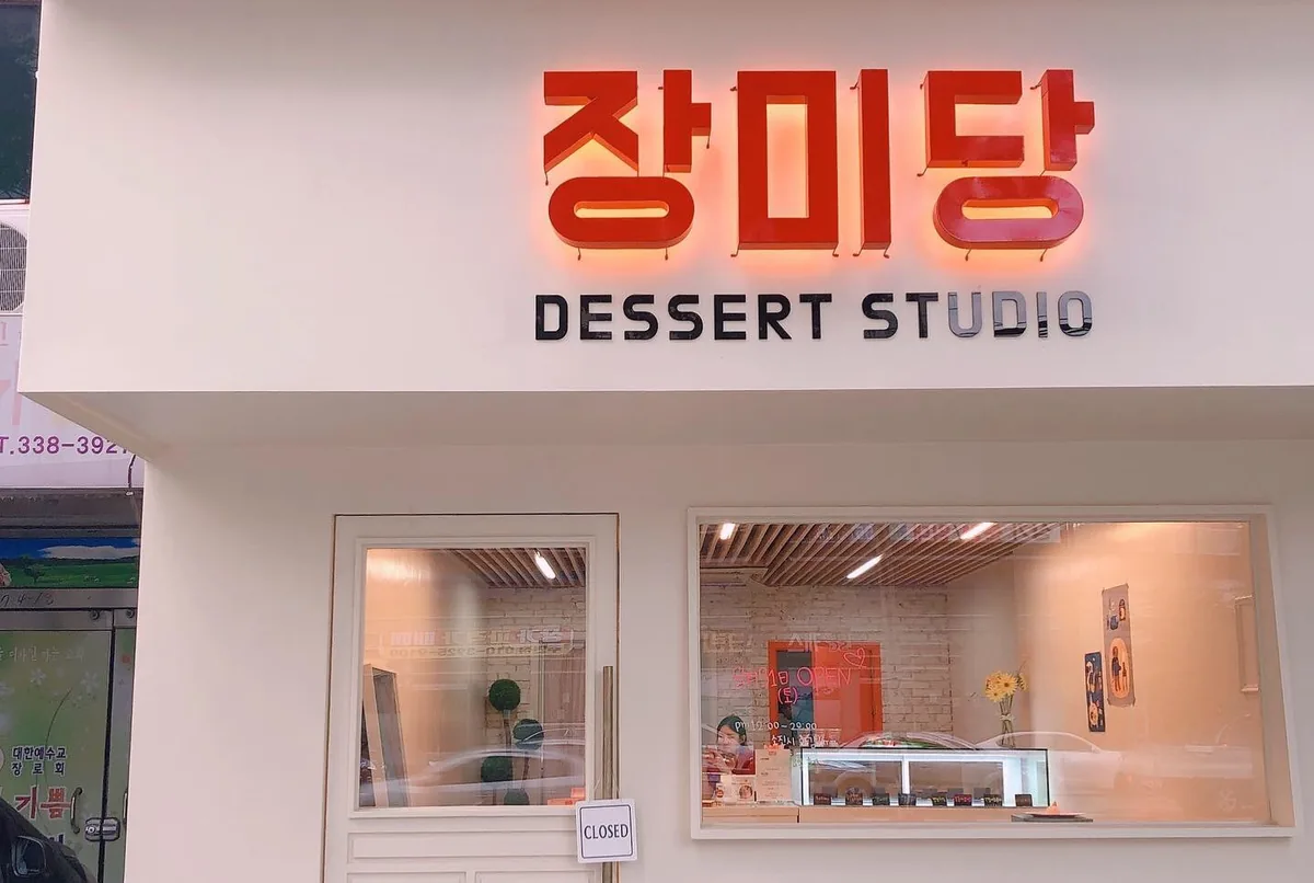 장미당 디저트스튜디오 매장 외관 — 붉은 「장미당」 간판과 흰 외벽, 입구와 진열창